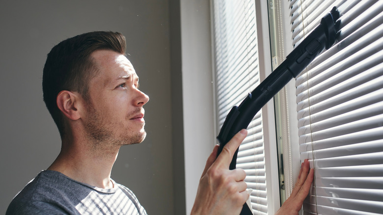 man vacuuming window blinds
