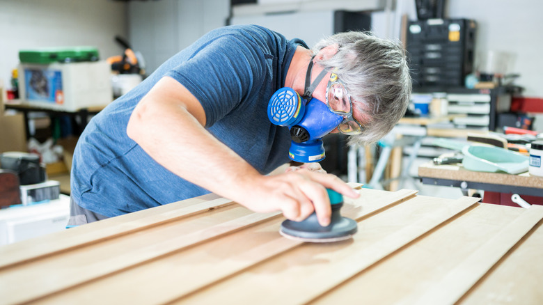 Man sanding wood while wearing mask