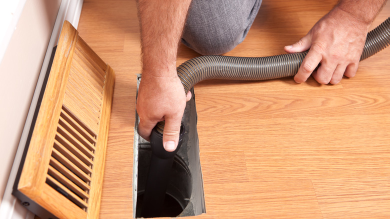 Man kneeling down on hardwood floor cleaning HVAC ducts