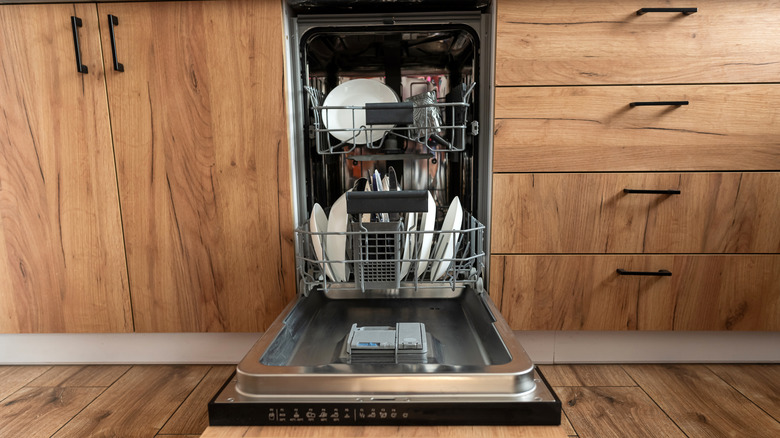 An open dishwasher fileld with dishes in a wooden kitchen