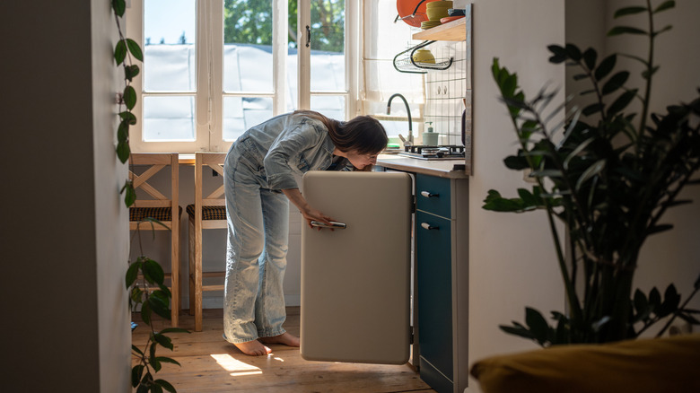 Woman looking inside under counter fridge.