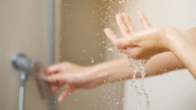 A person puts their hand under the shower with running water dripping down