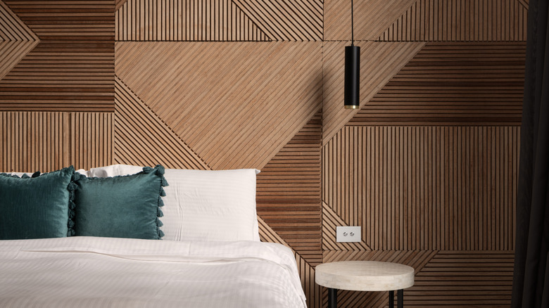 An intricate wood accent wall behind a white bed with blue throw pillows