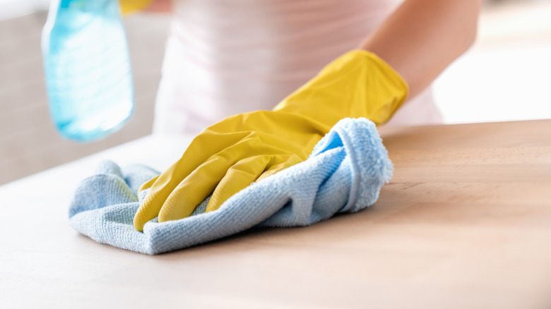 A gloved hand using a microfiber cloth to dust wood