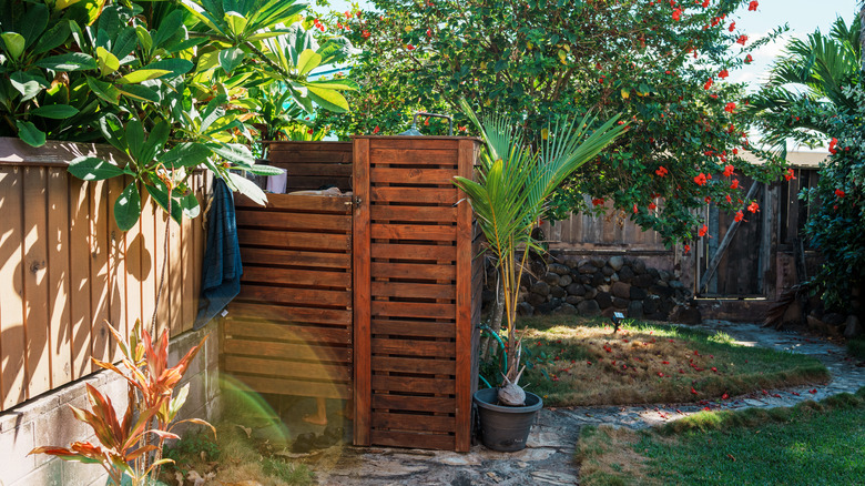 A wooden outdoor shower encloser with trees and plants around it