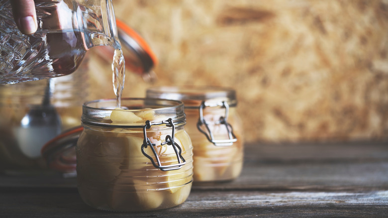 Hand pouring water into canning jar with apples