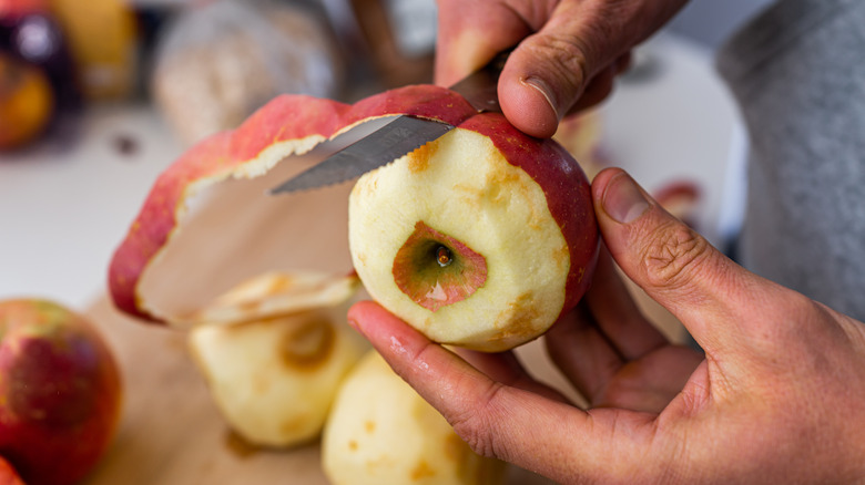 Person's hands peeling red apple with a knife