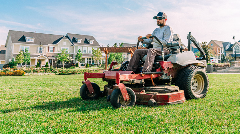 Man on zero-turn mower cutting large field with houses in the background