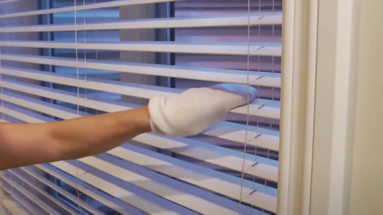 person cleaning blinds with sock