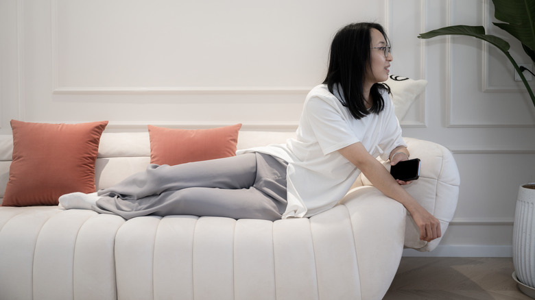 Woman with phone lounging on a curved contemporary white sofa.