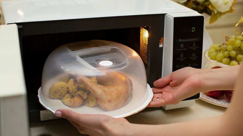 person putting a plate of chicken in the microwave