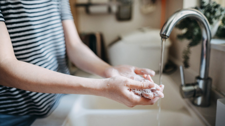 Woman in black and white striped shirt washing her hands with soap and water at a kitchen sink