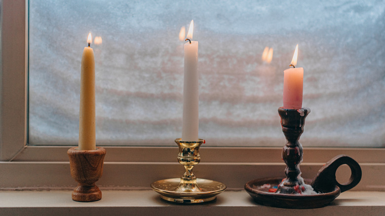 Three candlesticks in holders in front of window