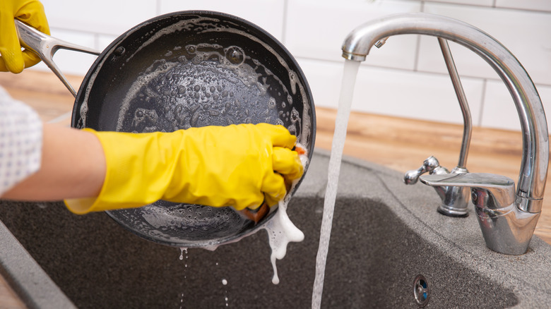 Person's hand cleaning burnt frying pan