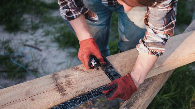 A man measures and cuts wooden planks