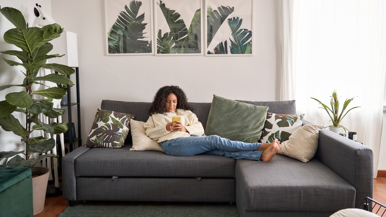 A young woman relaxes on a comfy lounge and scrolls through images on her phone.