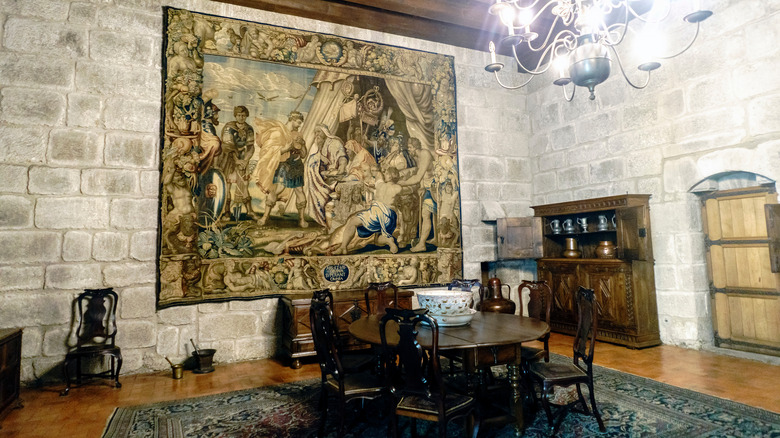 A large tapestry hangs on a stone wall over a round table in a medieval estate in Portugal