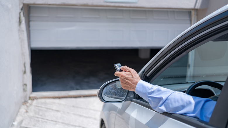 Hand through car window using remote to open garage door