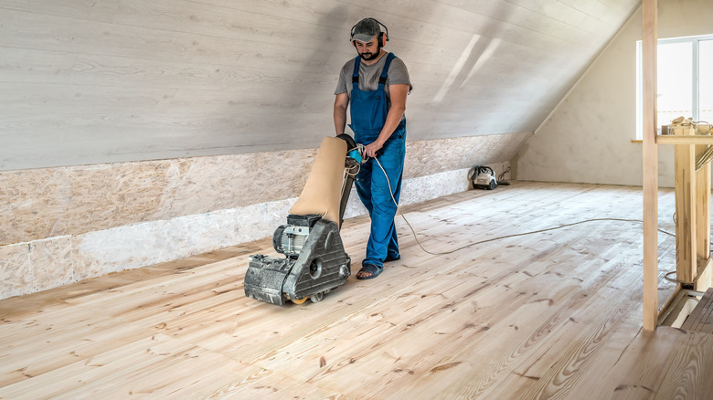 Man in overall sanding hardwood floor with drum sander