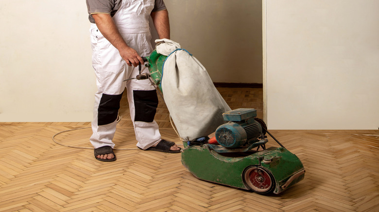 Man sanding a hardwood floor while wearing a respirator