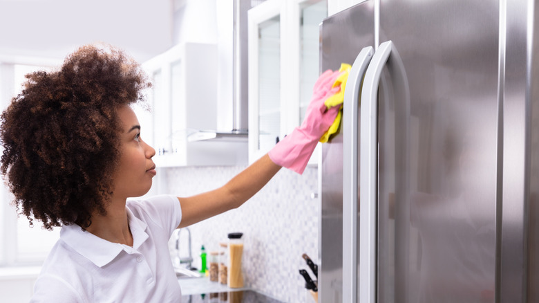 Woman wiping stainless steel refrigerator