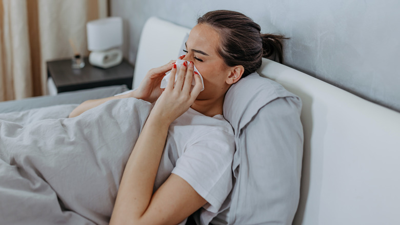 woman blowing nose in bed