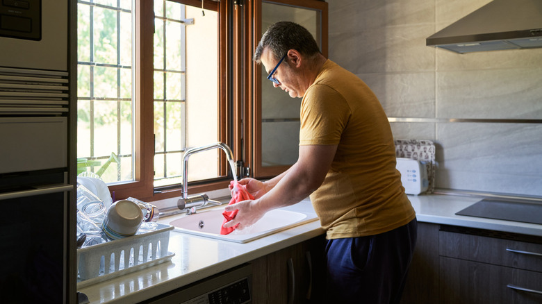 A man rinses a washcloth in a kitchen sink