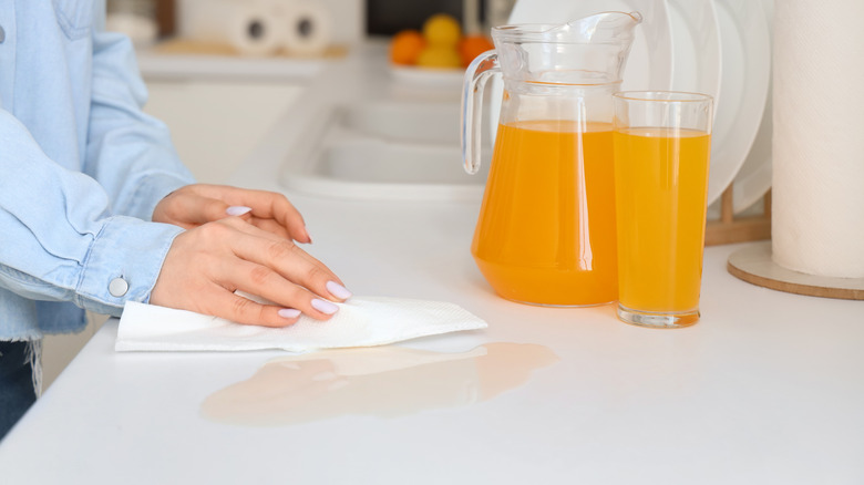 A woman wipes up spilled juice on a white countertop