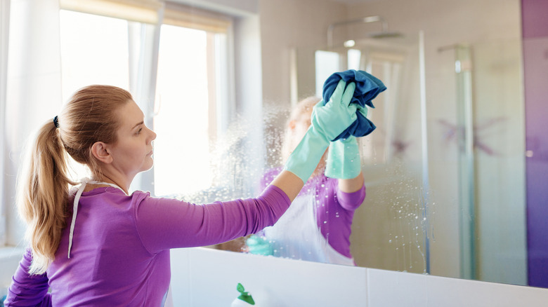 Woman cleans mirror with cloth